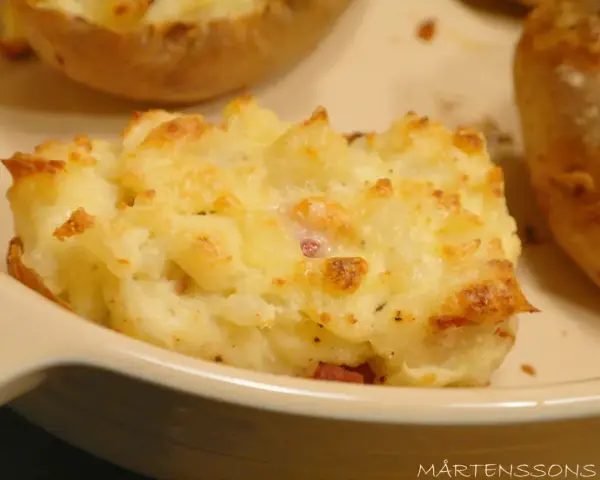 En närbild på en krämig, osttäckt bakad potatis fylld med baconbitar.