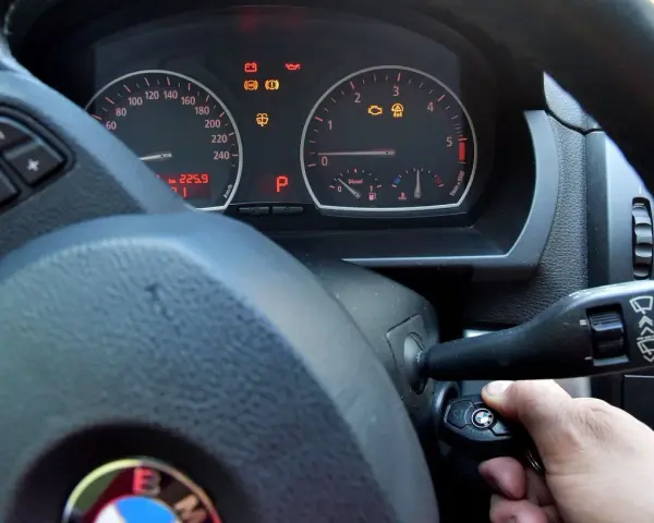 Ręka wsuwa kluczyk do stacyjki, by dowiedzieć się, jak odpalic auto. Na desce rozdzielczej świecą kontrolki.