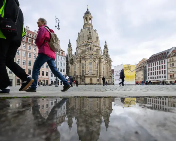 Menschen spazieren über einen nassen Platz vor der Frauenkirche, ein Symbol für offene Kirchen.