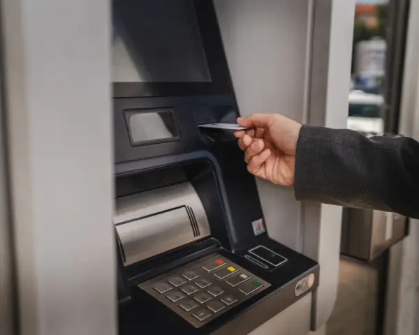 Dłoń wsuwa kartę do bankomatu, by sprawdzić, ile można wypłacić.
