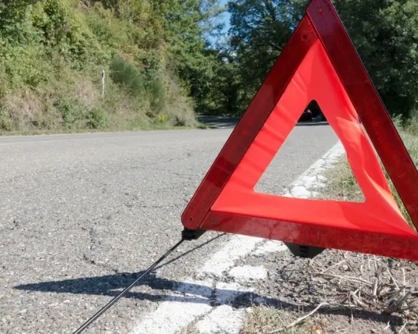 Czerwony trójkąt ostrzegawczy odległości stoi na poboczu drogi, sygnalizując awarię.