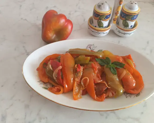 Piatto di peperoni alla siciliana, colorati e saporiti, con un peperone crudo sullo sfondo e saliere decorate.