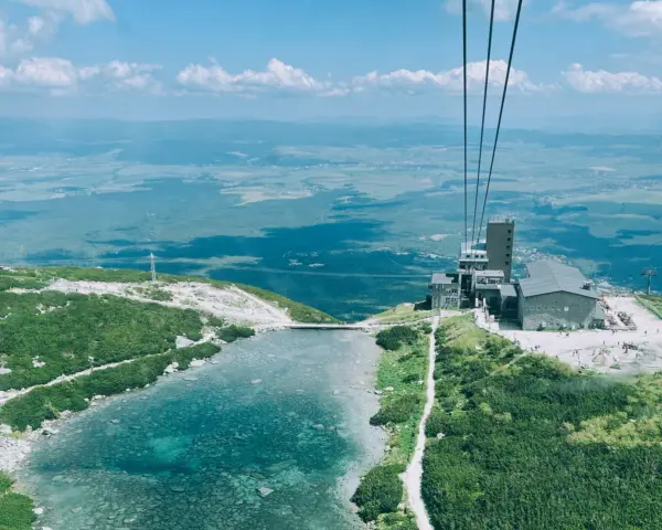 Widok z kolejki linowej na Skalnate Pleso, drugi szczyt w Tatrach. Jezioro, budynek i rozległa panorama.