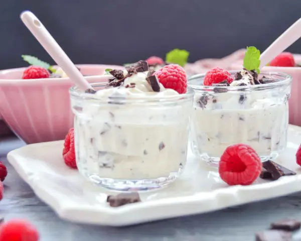 Zwei Gläschen mit cremigem Dessert, garniert mit Himbeeren und Schokostückchen. Ein köstliches Herrencreme Rezept zum Genießen.