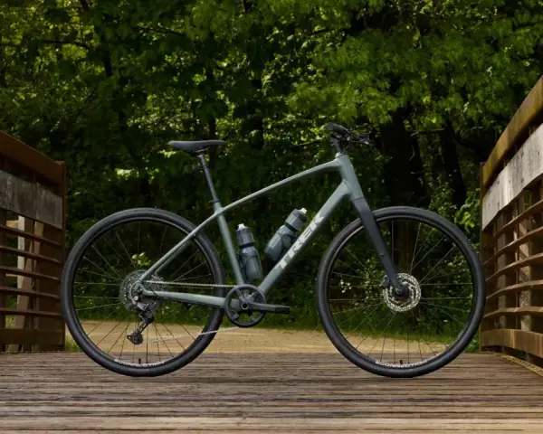 A grey Trek bike sits on a wooden bridge, ready for road or mountain biking adventures through the lush green forest.