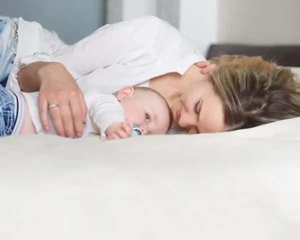 Mama tuli tuląca dziecko, ucząc się jak odkładać dziecko do łóżeczka, by spało spokojnie.