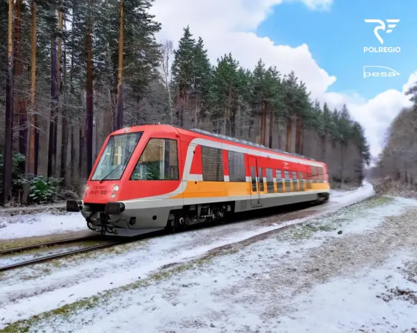 Czerwono-żółty pociąg EN 81-005 Polregio mknie przez zaśnieżony las.