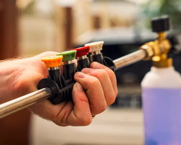Choosing the right nozzle to pressure wash car is key. This hand holds a selection of colored tips for a pressure washer wand, ready for detailing.