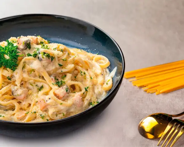 Pasta cremosa con trozos de salmón y perejil, servida en un plato azul oscuro.
