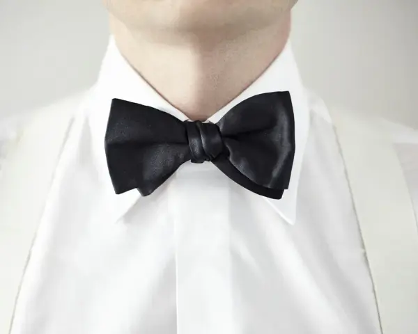 Elegancki mężczyzna w białej koszuli z czarną muszką i białymi szelkami. Kołnierzyk półwłoski idealnie dopełnia stylizację.
