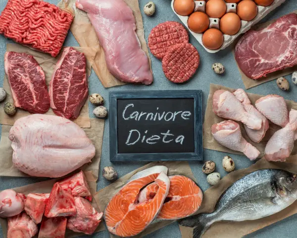 Różnorodne mięsa, ryby i jaja na stole. Tabliczka z napisem "Carnivore Dieta" sugeruje inspiracje kulinarne dla tej diety.