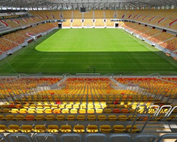 Pusta trybuna stadionu Jagiellonii, z żółtymi i czerwonymi siedzeniami. Pojemność obiektu robi wrażenie.