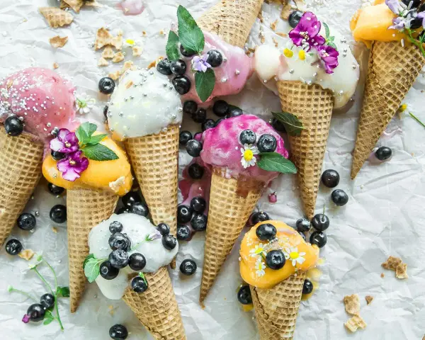 Bunte Eistüten mit Blaubeeren und Blüten. Wer fragt sich, wie viel Kalorien hat eine Kugel Eis, wenn sie so verlockend aussieht?
