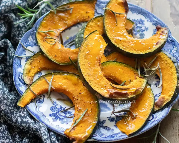 Fette di zucca in friggitrice ad aria, dorate e profumate al rosmarino, servite su un piatto blu e bianco.