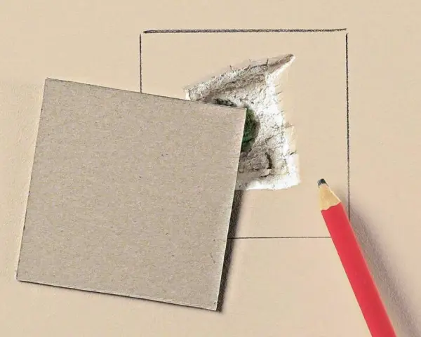 Kartonowy plaster i ołówek czekają, by pokazać, jak załatać dużą dziurę w ścianie.