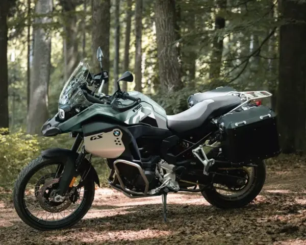 Zielony motocykl BMW F900GS z kuframi, gotowy na przygodę w lesie.