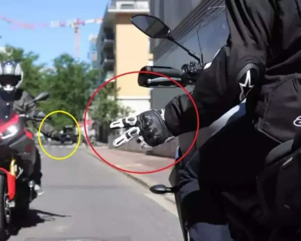 Mano guantata che fa il segno di pace, un gesto del linguaggio motociclisti. Un'altra moto in lontananza.
