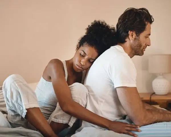 Un couple assis dos à dos sur un lit, l'air distant. On ne peut plus se parler sans s'engueuler.