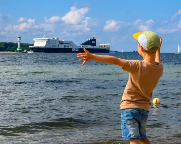 Kind winkt einem großen Schiff in Flensburg zu. Ein toller Ausflug mit Kindern, auch wenn es mal regnet.