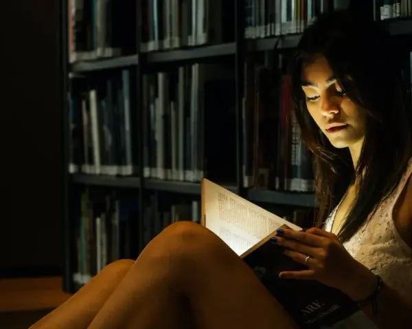 Elena, in the library's dim light, engrossed in a book.