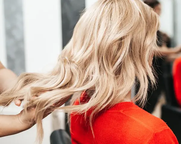 Fryzjerka pokazuje klientce, jak obciąć włosy, prezentując pasmo blond włosów.