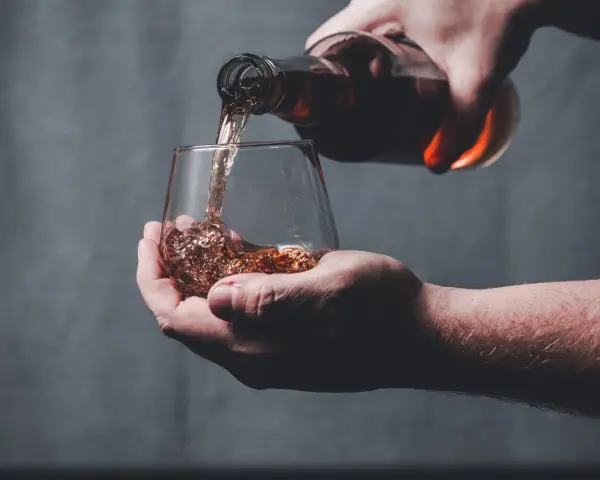 Dłoń nalewa bursztynowy płyn z butelki do szklanki. Czy whisky to bimber?