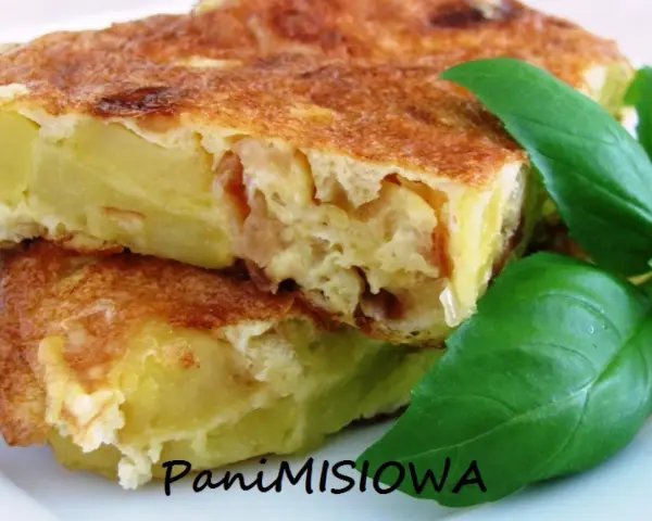 Pyszna tortilla de patatas, ze złotobrązową skórką i soczystym wnętrzem, ozdobiona świeżymi liśćmi bazylii.