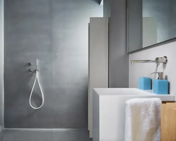 Bagno moderno con rivestimento doccia senza piastrelle effetto resina, lavabo bianco e accessori azzurri.
