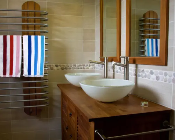 Salle de bain moderne avec double vasque. L'arrivée d'eau est discrète, deux lavabos blancs reposent sur un meuble en bois. Deux serviettes rayées sèchent sur un radiateur.