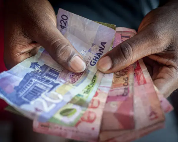 Dłonie trzymające banknoty cedi Ghany o różnych nominałach.