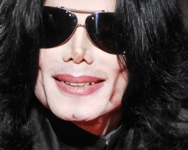 Michael Jackson w okularach przeciwsłonecznych i czarnych włosach. Jego uśmiech i twarz budzą pytania, jak zmarł Michael Jackson.