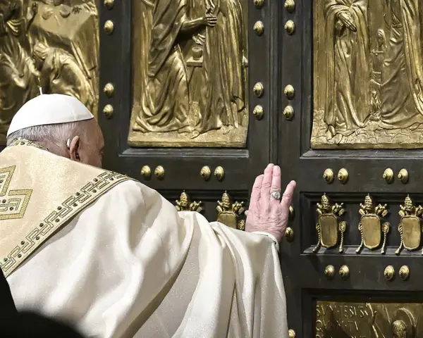 Papst Franziskus berührt die heilige Pforte des Petersdoms. Die bronzene Tür ist mit Reliefs verziert, die biblische Szenen darstellen.