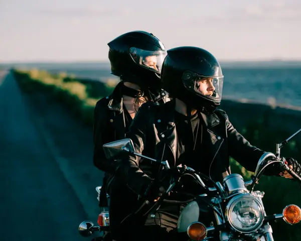 Coppia in moto romantica, con caschi neri, giacche di pelle, su una strada panoramica al tramonto.