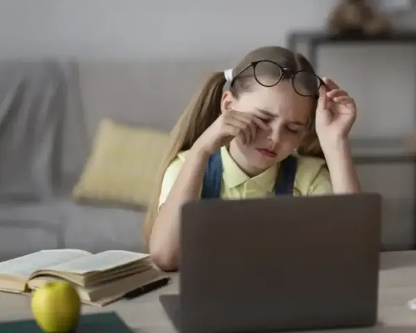 Zmęczona dziewczynka z okularami na czole pociera oczy, ucząc się przy laptopie. Jej indywidualna ścieżka nauczania jest trudna.