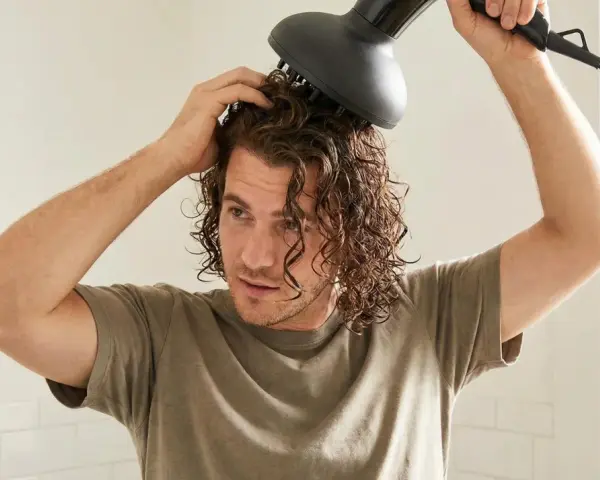 Ein junger Mann mit wellen haaren föhnt sich die Locken mit einem Diffusor.