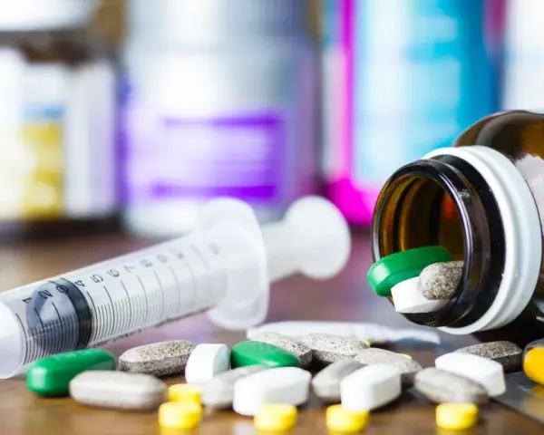 Leki, w tym zielone tabletki, rozsypane obok strzykawki i buteleczki. Może to być methocarbamol.