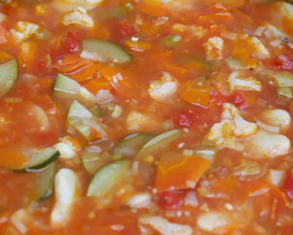 Gęsta, aromatyczna zupa jarzynowa, przypominająca włoskie minestrone, z kawałkami marchewki, cukinii i kalafiora w pomidorowym sosie.