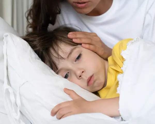 Chore dziecko w łóżku, mama głaszcze je po czole. Warto pamiętać o odpowiednich paracetamol czopki dawki dla dzieci.
