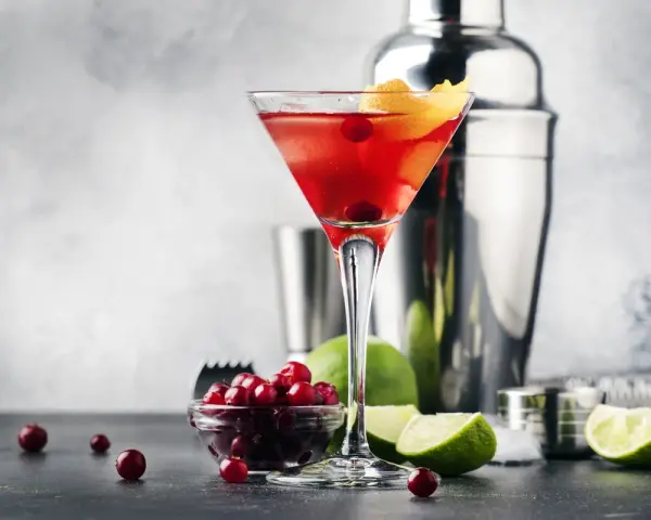 Elegancki cosmopolitan drink, gdzie zamiast żurawiny użyto świeżych owoców. Obok kieliszka stoją limonki i shaker.