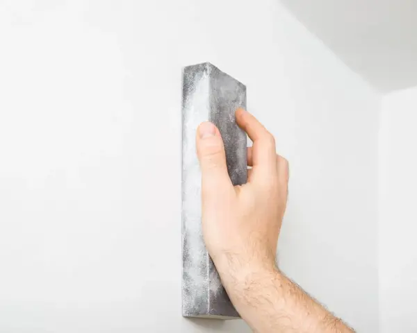 Mano lijando una pared blanca para reparar grietas en techo de yeso.