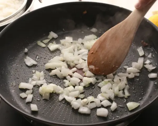 Cebolla picada se sofríe en una sartén, parte de unas deliciosas recetas con cebolla. Arroz blanco y mariscos esperan.