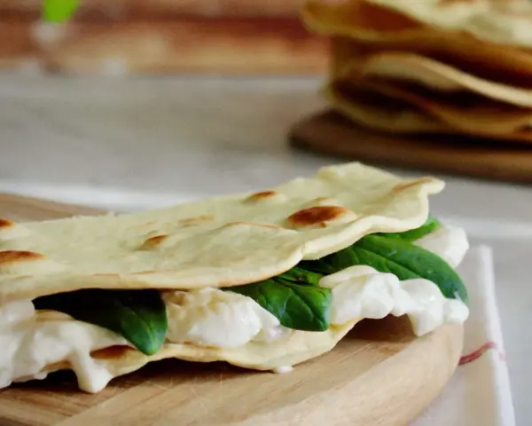 Piadina fatta in casa ripiena di mozzarella filante e spinacini freschi, pronta per essere gustata.
