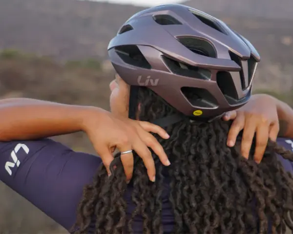 Donna con dreadlocks che regola un casco da bici Liv. Non preoccuparti se il tuo casco è stretto, ci sono modi per allargare il casco stretto.