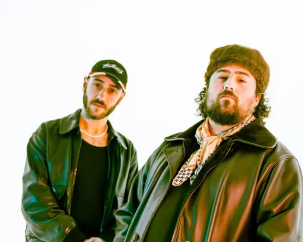 Deux DJ les plus connus, l'un porte une casquette et l'autre un bonnet en fourrure, posent devant un fond blanc.