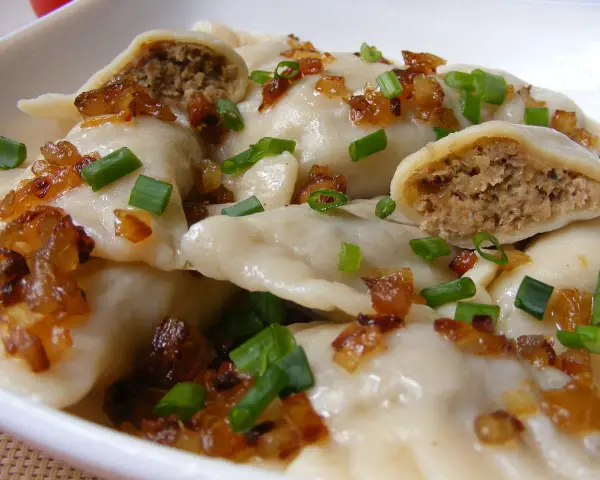 Domowe pierogi z mięsem, posypane smażoną cebulką i szczypiorkiem.