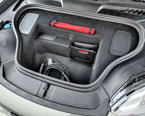 Otwarty bagażnik Porsche Macan z kablem do ładowania, apteczką i instrukcją.