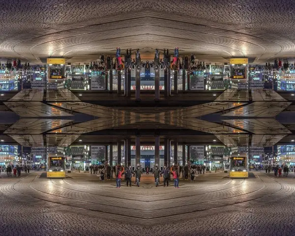 Nocne miasto z żółtym tramwajem i ludźmi. Kompozycja symetryczna tworzy surrealistyczny, odbity świat.