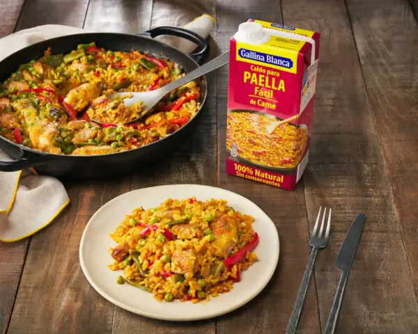 Paella de carne recién hecha en sartén y plato, lista para disfrutar. Un caldo Gallina Blanca para paella fácil de carne a su lado.