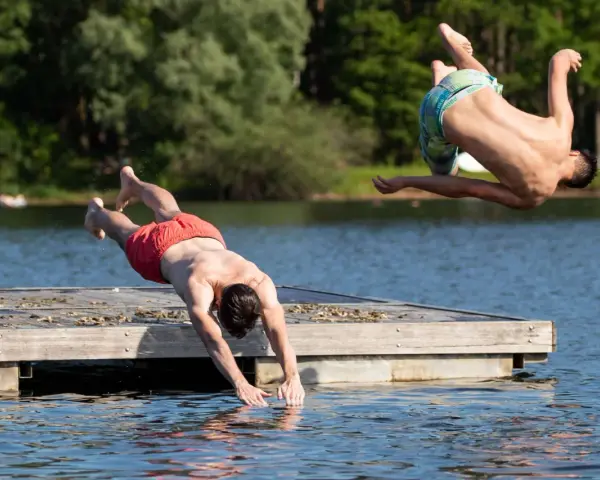 Zwei Männer springen vom Steg in den Sieglarer See. Einer macht einen Salto, der andere taucht gerade ins Wasser.