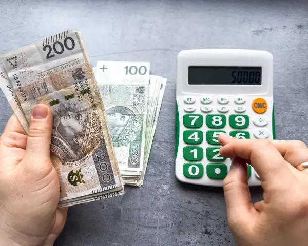 Ręka z polskimi banknotami 200 zł i 100 zł obok kalkulatora z wyświetloną kwotą 50000. Planowanie waloryzacji emerytury 2026.